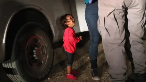 Getty Images A two-year-old Honduran girl as her mother is searched and detained near the US-Mexico border on in McAllen, Texas, on 12 June 2018