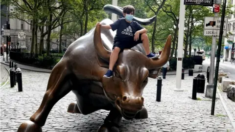 Reuters A child wearing a face mask sits on the Charging Bull statue, also known as the Wall St. Bull, following the outbreak of the coronavirus disease (COVID-19) in the Manhattan borough of New York City, New York, U.S., August 19, 2020