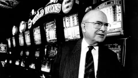 Getty Images Len Ainsworth standing in front of a row of pokies machines