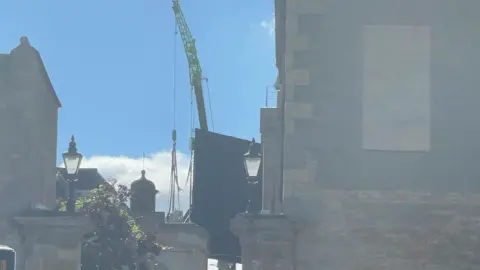 A large blackboard hanging from a crane in front of windows at Burghley House