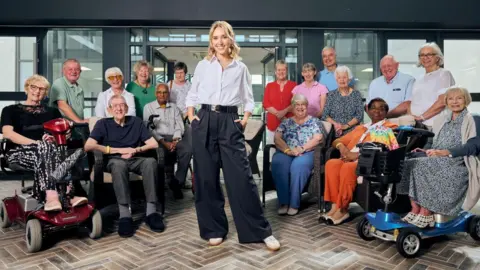 Rogan Productions Rose Ayling-Ellis stands in the middle of the picture surrounded by people who live in the retirement village and have taken part in the show 