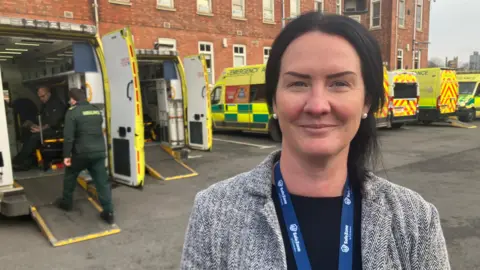 A woman stood outside a hospital with an ambulance crew climbing into their vehicle behind her