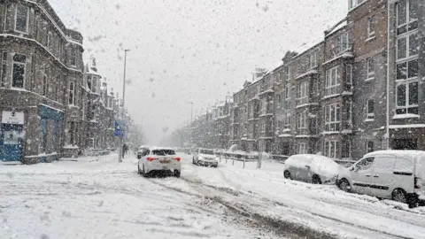 PA Media Big flakes of snow fall on a snow-covered street in Inverness on 5 January this year.
