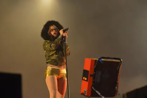 Getty Images A female singer in gold shorts and a camouflage jacket with a fur hood