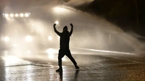 Charles McQuillan Silhouette of young person in front of water canon
