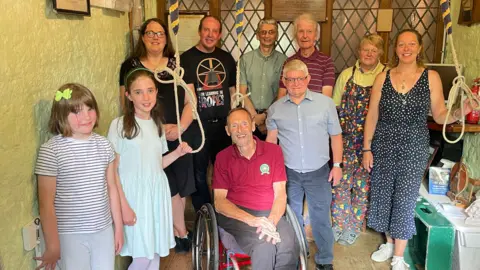 Mike sits in the middle of the tower in his wheelchair surrounded by bellringers holding ropes.