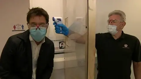 BBC A worker at the plants demonstrates how he would take someone's temperature