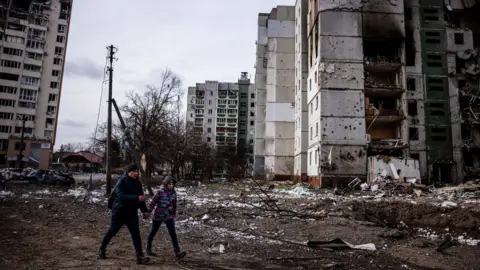 Getty Images Residents walk in front of residential buildings damaged in shelling in Chernihiv on 4 March