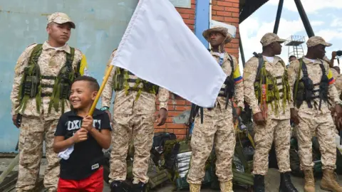 Getty Images A boy holds a white flag next to a group of members of the Farc guerrilla who arrived in Buenaventura, Colombia, on February 4, 2017