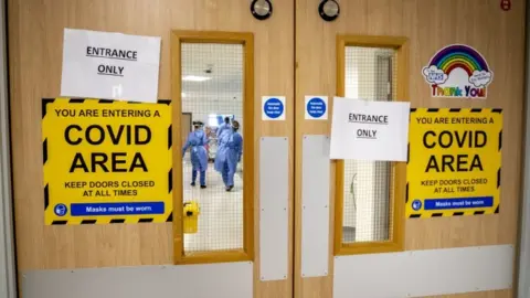 PA Media Medical staff behind a door with sign - You are entering a Covid Area.