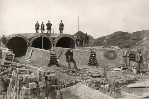 Otto Herschan Joseph Bazalgette, standing top right, views the Northern Outfall sewer being built below the Abbey Mills pumping station in 1862