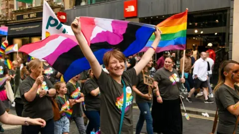 Haydn Brown/Northern Pride  Paraders smile at the camera as they wave bannes