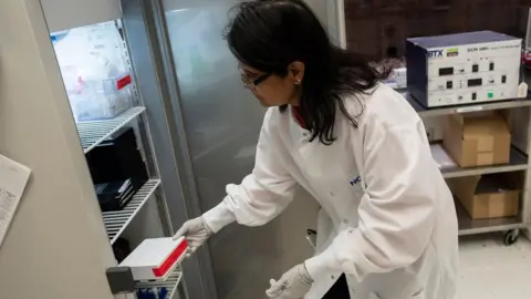 Getty Images Dr Nita Patel, Director of Antibody discovery and Vaccine development, returns a box of potential coronavirus vaccines to a fridge at Novavax labs in Gaithersburg, Maryland on 20 March, 2020