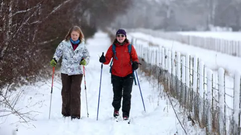 Getty Images Two people use skis and walking poles to trek through a snowy path next to a snow-covered fence with trees in the background, in Banchory, Scotland on Friday.