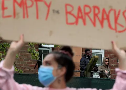 PA Media Asylum seekers watch a protest outside Napier Barracks