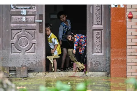 AFP Children remove water from inside their house in Longkou village due to torrential rains in Poyang county, Shangrao city, in China's central Jiangxi province on 16 July 2020