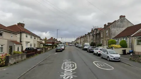 A Google Maps street view of Bishopsworth Road in Bristol. Houses line both sides of the residential street and cars can be seen parked up on both side of the relatively wide road.