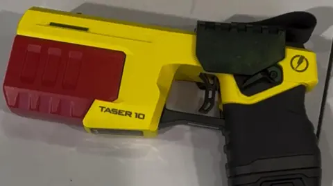 West Midlands Police and Crime Commissioner General view of a yellow and red taser with a black handle lying on a grey table.