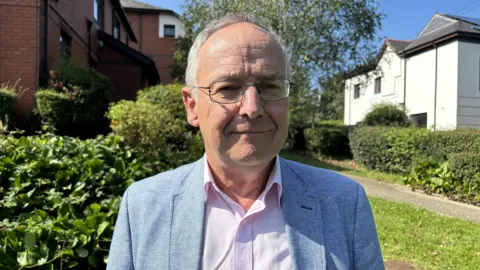 Council leader Dyfrig Siencyn wearing light blue jacket and standing in a garden