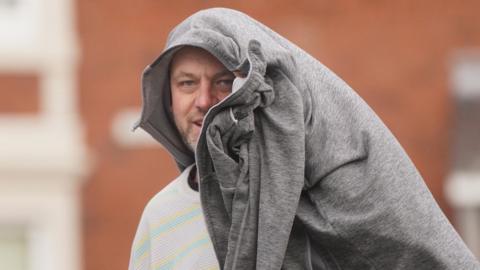 A man walks out of court with a grey jacket covering most of his head