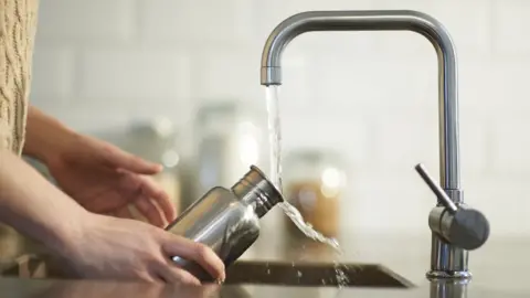 Getty Images A woman cleans a water bottle in a kitchen sink