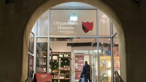 BBC The front of Chippenham museum's entrance showing the lit-up archway and glass door on a dark night