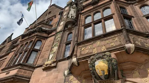 External view of Coventry City Council's headquarters. The council cot of arms is engraved into a sandstone building with ornate windows.
