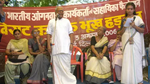 Getty Images Achuthanandan visto se dirigindo ao Standing on Stage, abordando uma manifestação de trabalhadores de saúde em Nova Délhi. Mulheres em saris sentam -se no palco ouvindo -o enquanto se fica segurando um microfone à direita