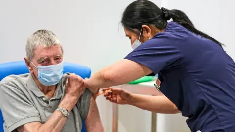 PA Media John Mason 82 receiving a Covid-19 vaccination from nurse Anie Santillan