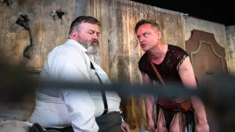 Tommy Ga-Ken Wan In character, Tom Urie sitting on a bed speaking to "Liz" played by Darren Brownlie