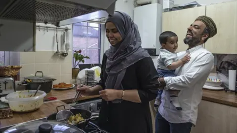 Getty Images Imam Raza Ahmed holds his son as his wife prepares food for iftar