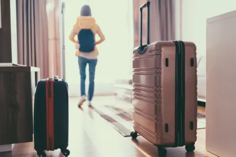 Getty Images Woman who has just entered hotel room with suitcases