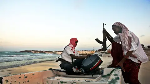 Getty Images Somali men with guns getting aboard a small boat