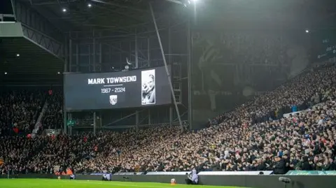 Getty Images A large screen with the words Mark Townsend and a black and white image in a packed football stadium