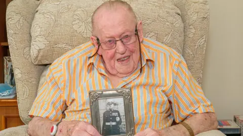 Postcode Lottery Bernard Botting holding a picture of himself as a marine.