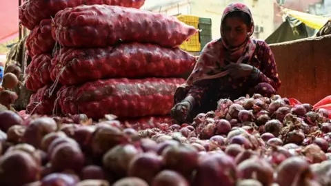 Getty Images A woman sorts out onions at a vegetable market in Delhi on May 30, 2023