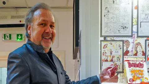 PA Media Dandy artist Nigel Parkinson next to his sketches and artwork of Beatle Sir Paul McCartney