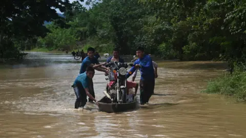 Getty Images People carry a motorbicycle on a boat in a flooded area in Panzos, Alta Verapaz