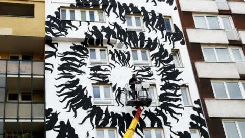 EPA The artist David de la Mano works on his street art painting on the outskirts of a residential house near the Museum for Urban Contemporary Art in Berlin (15 September 2017)