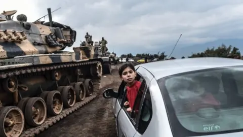 AFP A Turkish girl leans out of a car window to have a look as Turkish army tanks and soldiers gather close to the Syrian border at Hassa, in Hatay province on 21 January 2018.