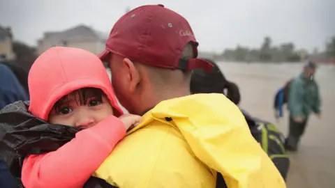 Getty Images A small child is held in a man's arms after being rescued from the floods.