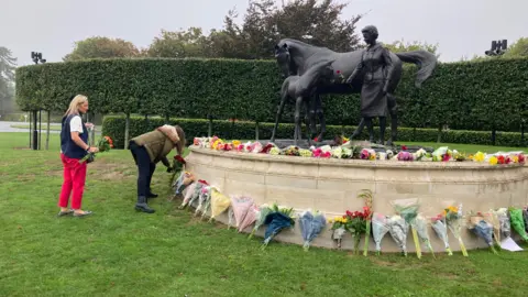 Rachael McMenemy/BBC People laying the flowers at the statue of the Queen in Newmarket