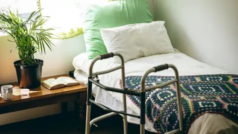 Wavebreakmedia The inside of a care home room with a walking frame and bed