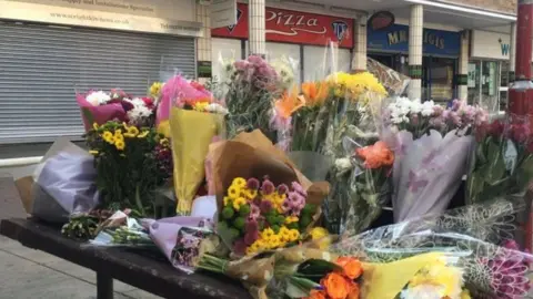 Flowers left near a row of shops in Harlow where a Polish man was attacked.