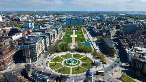 Hull College An aerial view of a city centre park in front of a large multi-storey college block, with blue and white cladding. 