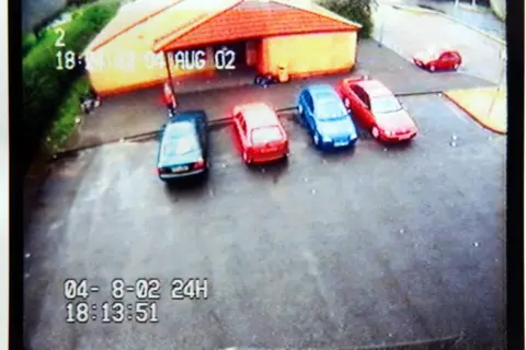 PA Media A CCTV still image taken from a camera looking down at a car park, with red and blue cars parked up. A figure wearing a red top is faintly visible.