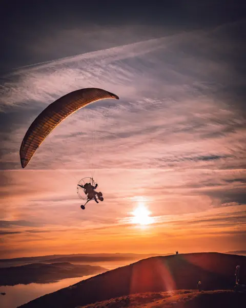 Luis Gonzalez Araujo Paraglider flying into a red orange sunset