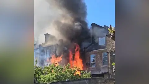 Flames and smoke can be seen pouring out of a tall London-style town house 