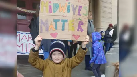 Claire Rudge Child holds sign reading 'midwives matter'