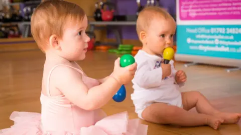 Emma Morgan Two babies sitting up and holding rattles at a Tiny Toes class